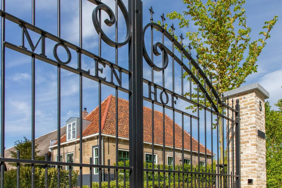 A gated entrance with the words 'MOLEN HOF' visible, leading to a building with a red-tiled roof and a stone tower.