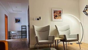 A modern living room with two armchairs, a glass coffee table, and a painting on the wall. - Noktel Resort Apartment  (Abuja)
