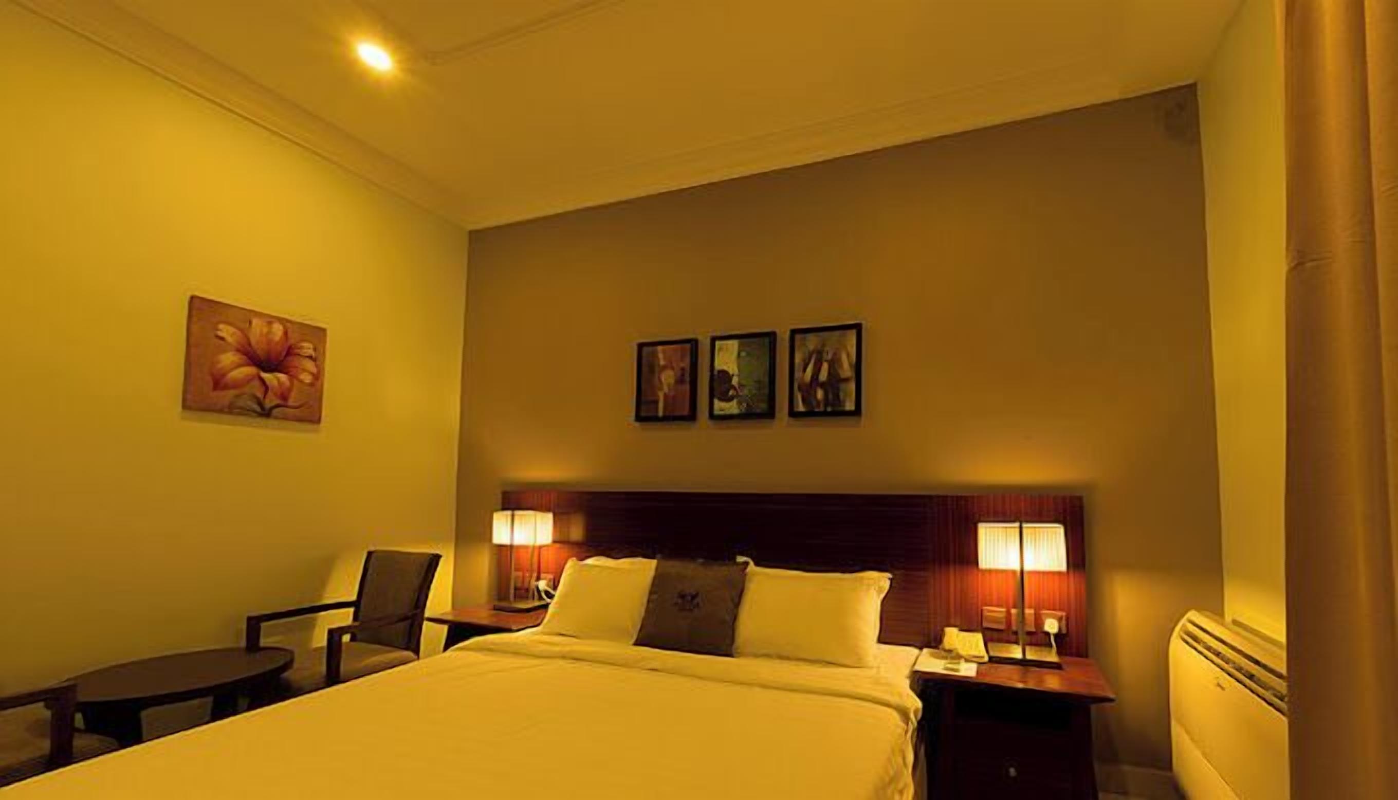 A hotel room with a large bed, two bedside tables with lamps, a chair, and three framed pictures on the wall.