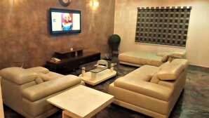 A living room with a sofa, armchairs, a coffee table, a TV, and a patterned window blind. - Noktel Resort Apartment  (Abuja)