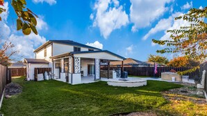 A two-story house with a covered patio, a well-maintained lawn, and a backyard with a fire pit. - Spacious Home with Gorgeous Backyard Kitchen, Close to Top Shopping Destinations (Leander)