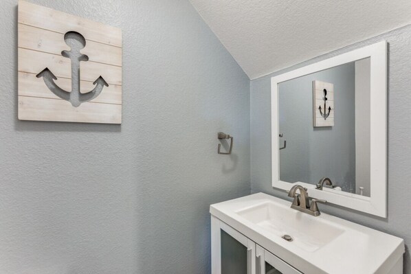 A bathroom with a white sink, a large mirror, and a wooden anchor decoration on the wall. - Spacious Home with Gorgeous Backyard Kitchen, Close to Top Shopping Destinations (Leander)