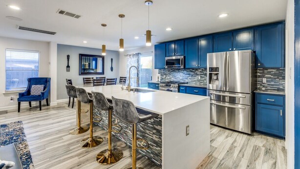 A modern kitchen with blue cabinets, stainless steel appliances, and a central island with bar stools. - Spacious Home with Gorgeous Backyard Kitchen, Close to Top Shopping Destinations (Leander)