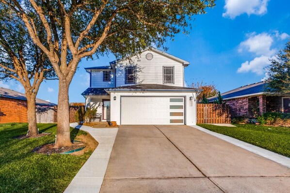 Una casa a due piani con garage, vialetto e un albero nel giardino antistante.