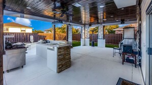 An outdoor patio with a stone island, a grill, and a ceiling fan. - Spacious Home with Gorgeous Backyard Kitchen, Close to Top Shopping Destinations (Leander)