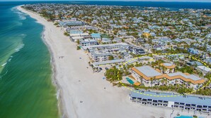An aerial view of a coastal residential area with beachfront properties, a swimming pool, and a clear view of the ocean.