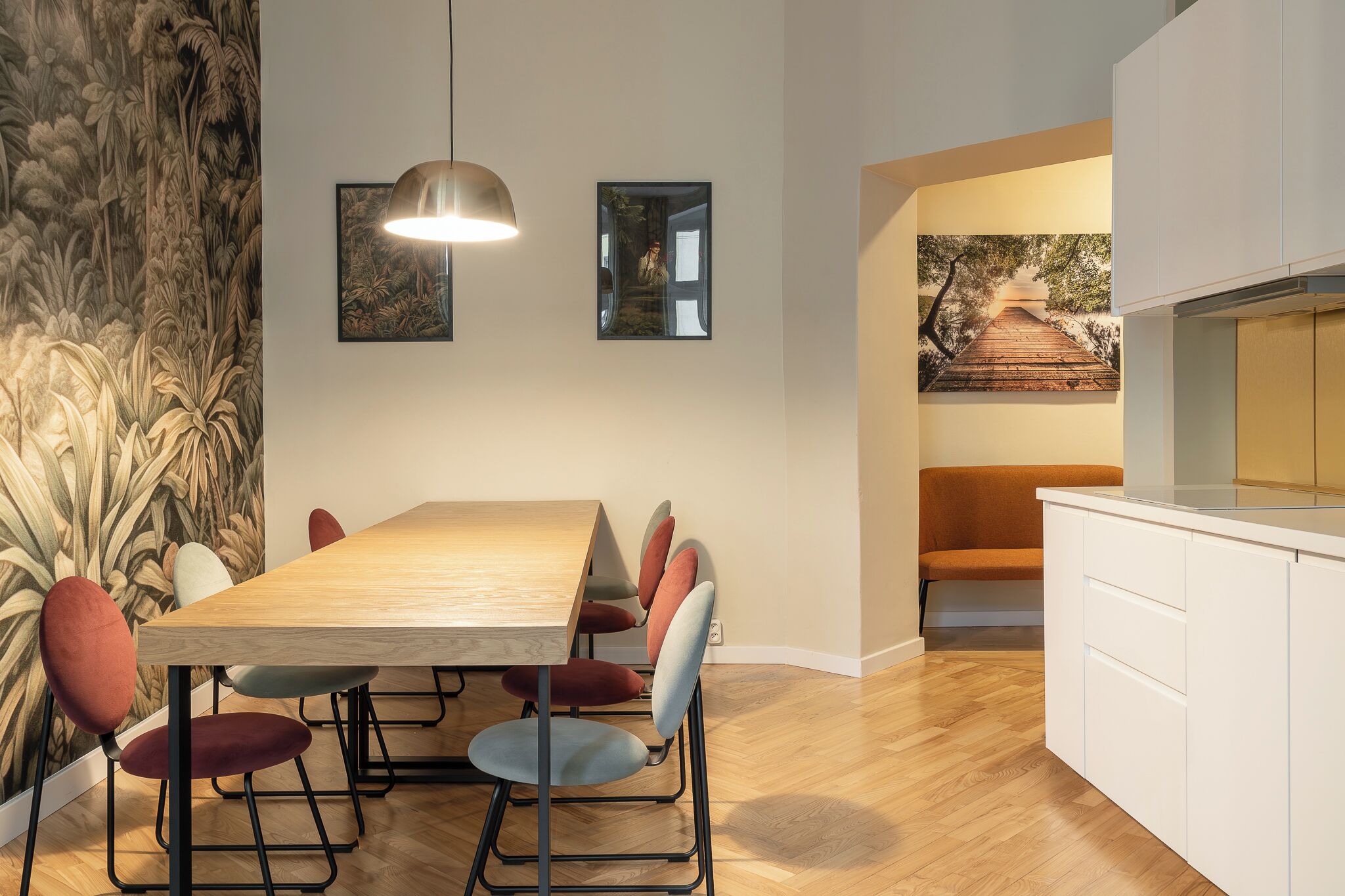 A modern dining area with a wooden table and chairs, a hanging light fixture, and a mural on the wall.