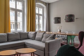 A modern living room with a sectional sofa, two round wooden tables, and a dining area with a wooden table and chairs. - RentPlanet - Apartament Nożownicza (Wroclaw)