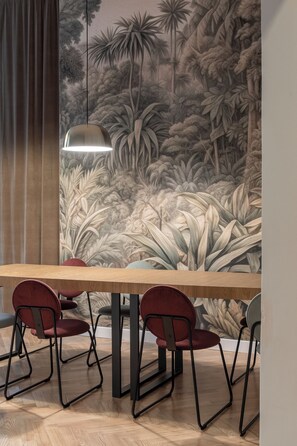 A dining area with a mural of a tropical forest, a wooden table, and red chairs. - RentPlanet - Apartament Nożownicza (Wroclaw)