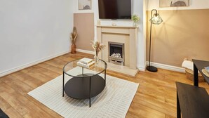 Een moderne woonkamer met een open haard, een flatscreen televisie erboven en een glazen salontafel.