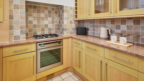 Een keuken met houten kastjes, een gasfornuis, een oven en een betegelde achterwand.