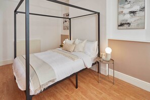 Un letto a baldacchino con copripiumino e cuscini bianchi, un comodino con lampada e un termosifone sullo sfondo.