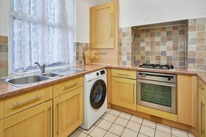 Una cocina con armarios de madera, lavadora, horno y pileta.