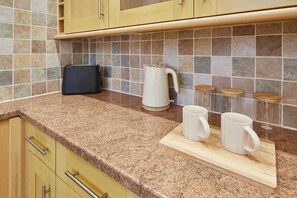 A kitchen with granite countertops, wooden cabinets, a coffee maker, and a cutting board with mugs.