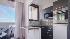 A modern kitchen with a built-in oven, microwave, and a small refrigerator. There is a dining area with a table and chairs, and a window with curtains. - Paris Expo 2 Residence (Paris)