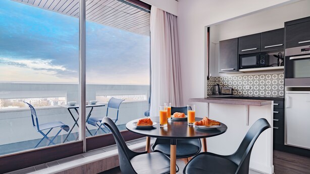 A modern dining area with a large window, a round table, and black chairs. - Paris Expo 2 Residence (Paris)