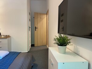 A bedroom with a bed, a dresser, a potted plant, and a door leading to another room. - Milla Apartments (Kraków)