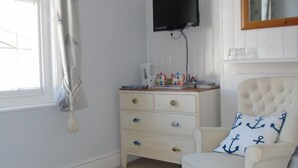 A room with a white dresser, a television mounted on the wall, a chair with a nautical pillow, and a window with curtains. - Cherry End bed and breakfast  (Chichester)