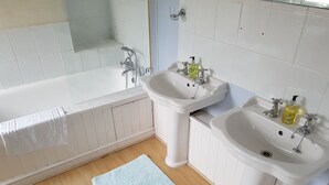 A bathroom with a bathtub, two sinks, a blue rug, and a shower area. - Cherry End bed and breakfast  (Chichester)