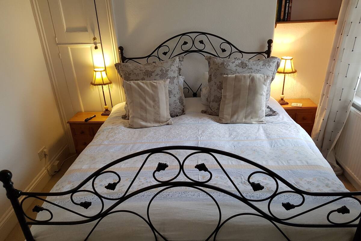 A neatly made bed with a floral-patterned bedspread and matching pillows, flanked by two bedside tables with lamps, in a room with a simple, clean design.