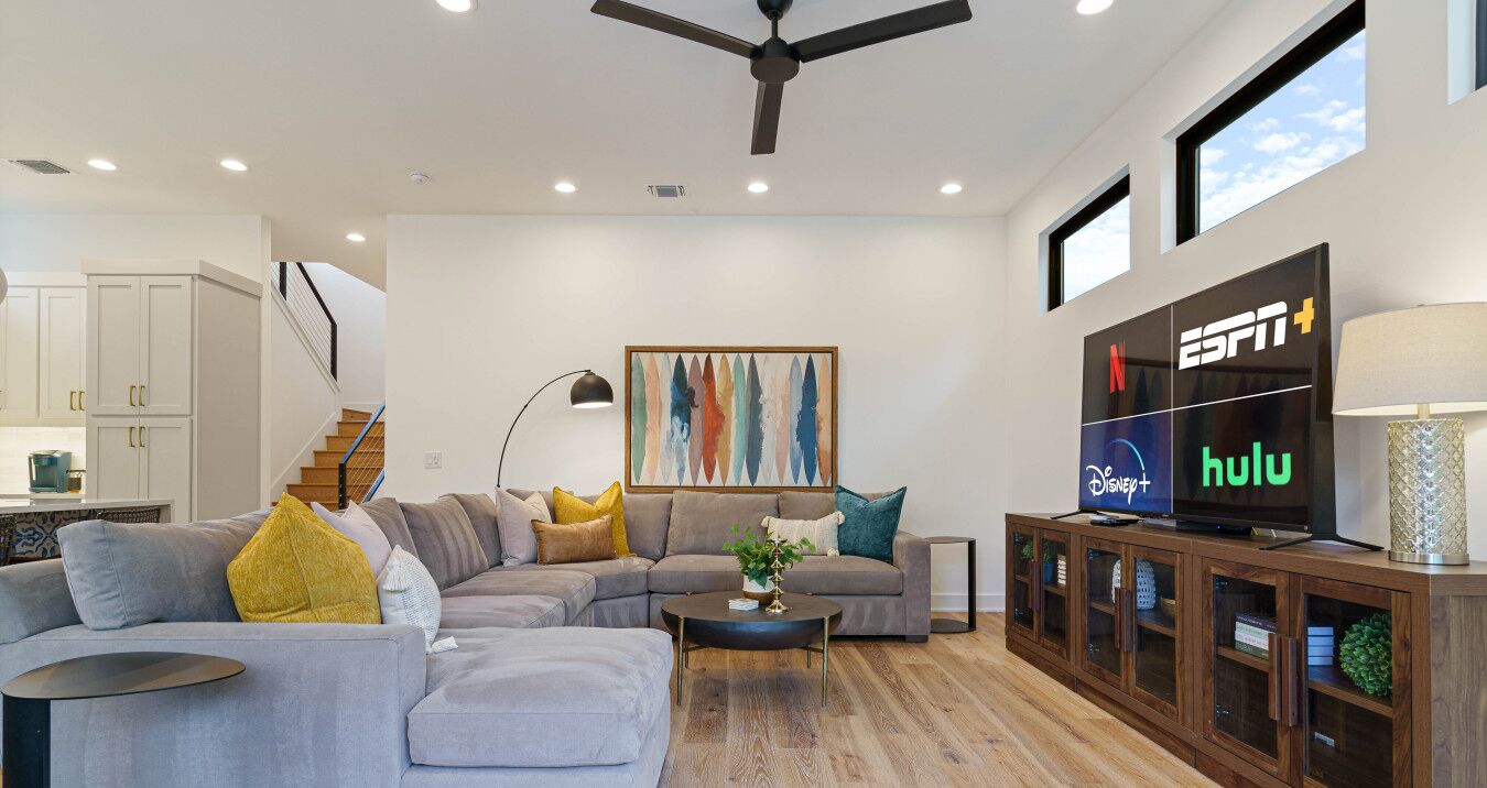 A modern living room with a sectional sofa, a coffee table, a TV displaying ESPN and Hulu, and a staircase leading to an upper level.