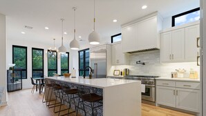 A modern kitchen with white cabinets, a large island with bar stools, stainless steel appliances, and pendant lighting. - 2605 E 4th xxxxxxxxx (Austin)