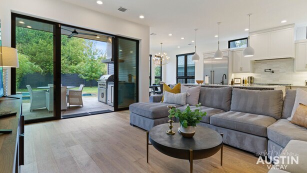 A modern living room with a grey sectional sofa, a round coffee table, and a sliding glass door leading to an outdoor patio with a grill. - 2605 E 4th xxxxxxxxx (Austin)
