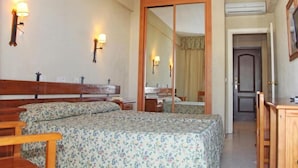 Une chambre d’hôtel avec un lit double, des tables de chevet, un miroir, une armoire et un petit bureau.