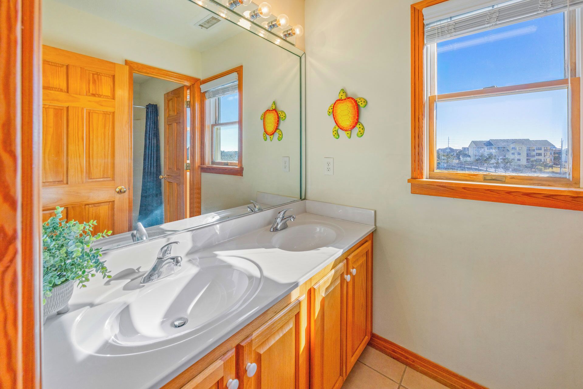A bathroom with a double sink, wooden cabinets, a large mirror, and a window with a view of buildings.