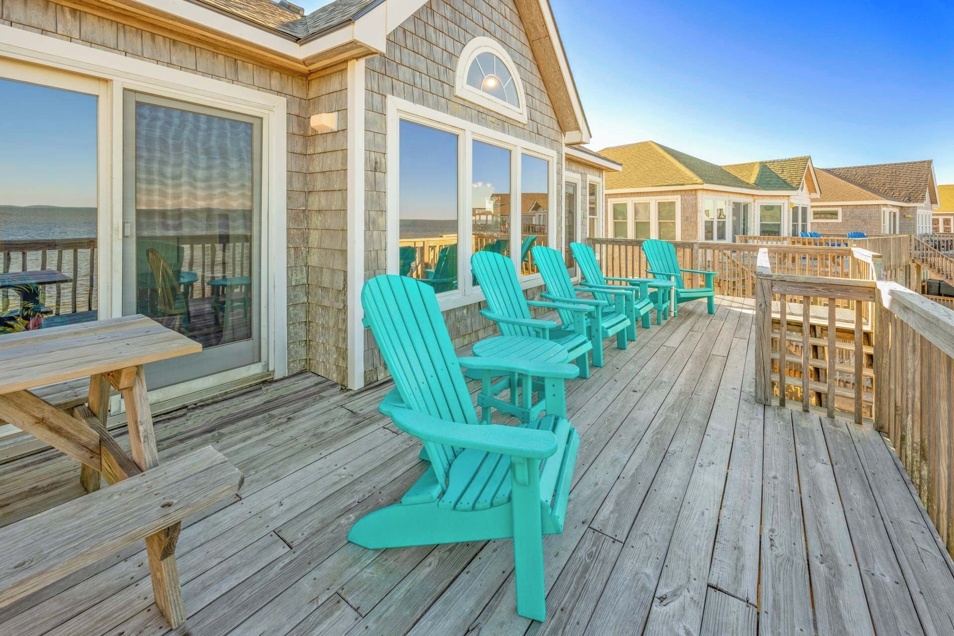 Une terrasse en bois avec des fauteuils Adirondack turquoise et une table, offrant une vue panoramique.