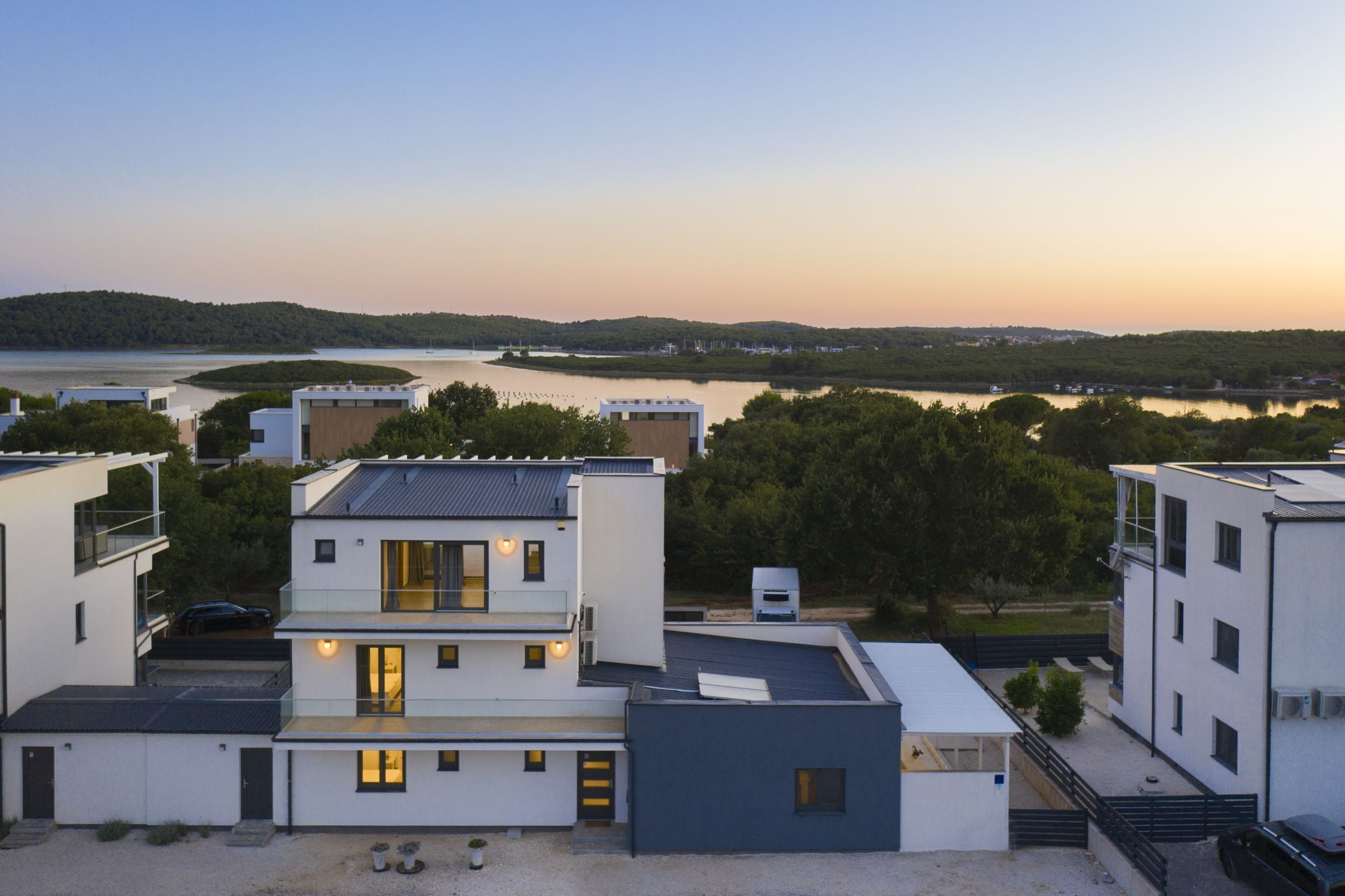 A modern residential area with multi-story buildings, a lake, and a forested hill in the background.