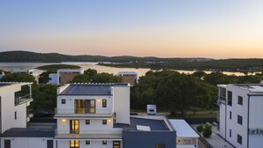 A modern residential area with multi-story buildings, a lake, and a forested hill in the background. - Elegant Villa Sole with private pool and sauna  (Pomer)