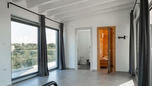 A modern hotel room with a large window, a wooden door leading to a bathroom, and a view of greenery outside. - Elegant Villa Sole with private pool and sauna  (Pomer)