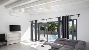 A modern living room with a grey sectional sofa, a white coffee table, a flat-screen TV, and a sliding glass door leading to a pool. - Elegant Villa Sole with private pool and sauna  (Pomer)