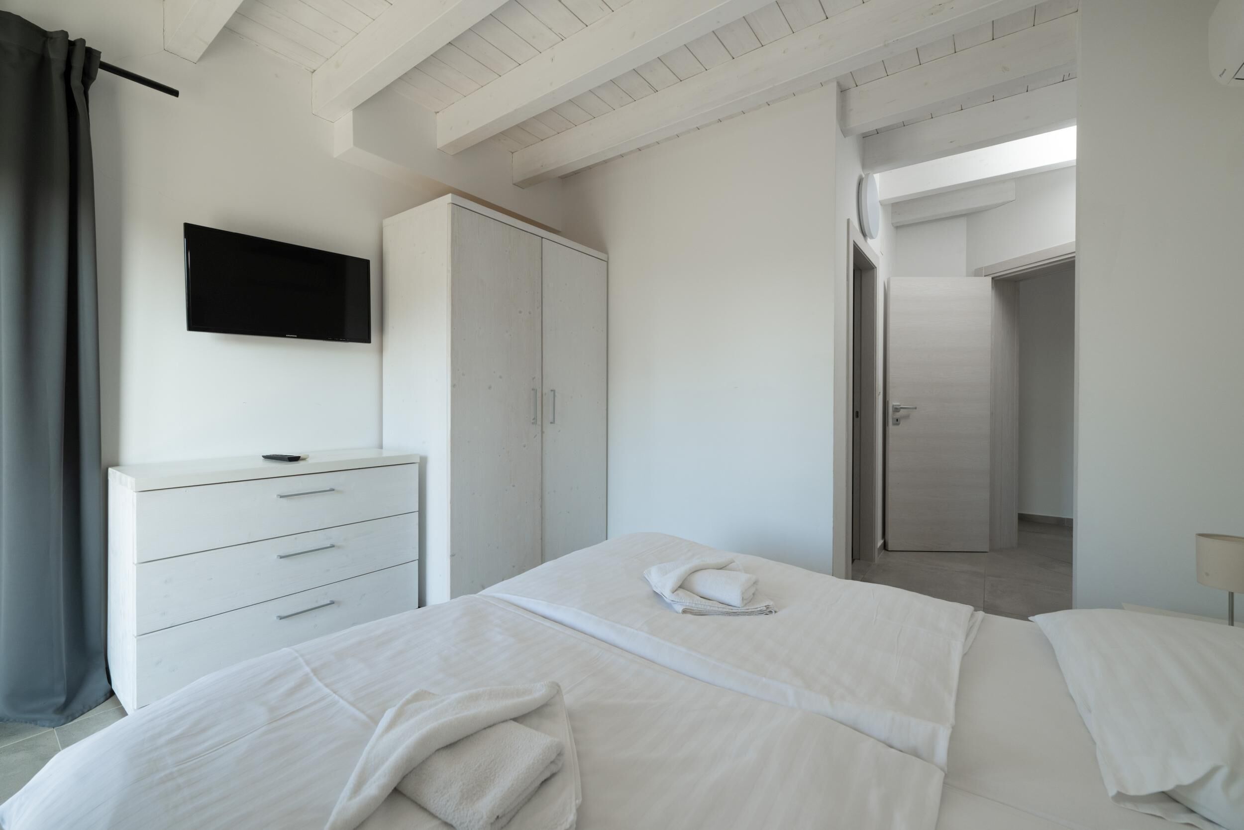 Ein Hotelzimmer mit Bett, Wandfernseher, Kleiderschrank und einer Tür zu einem weiteren Raum.