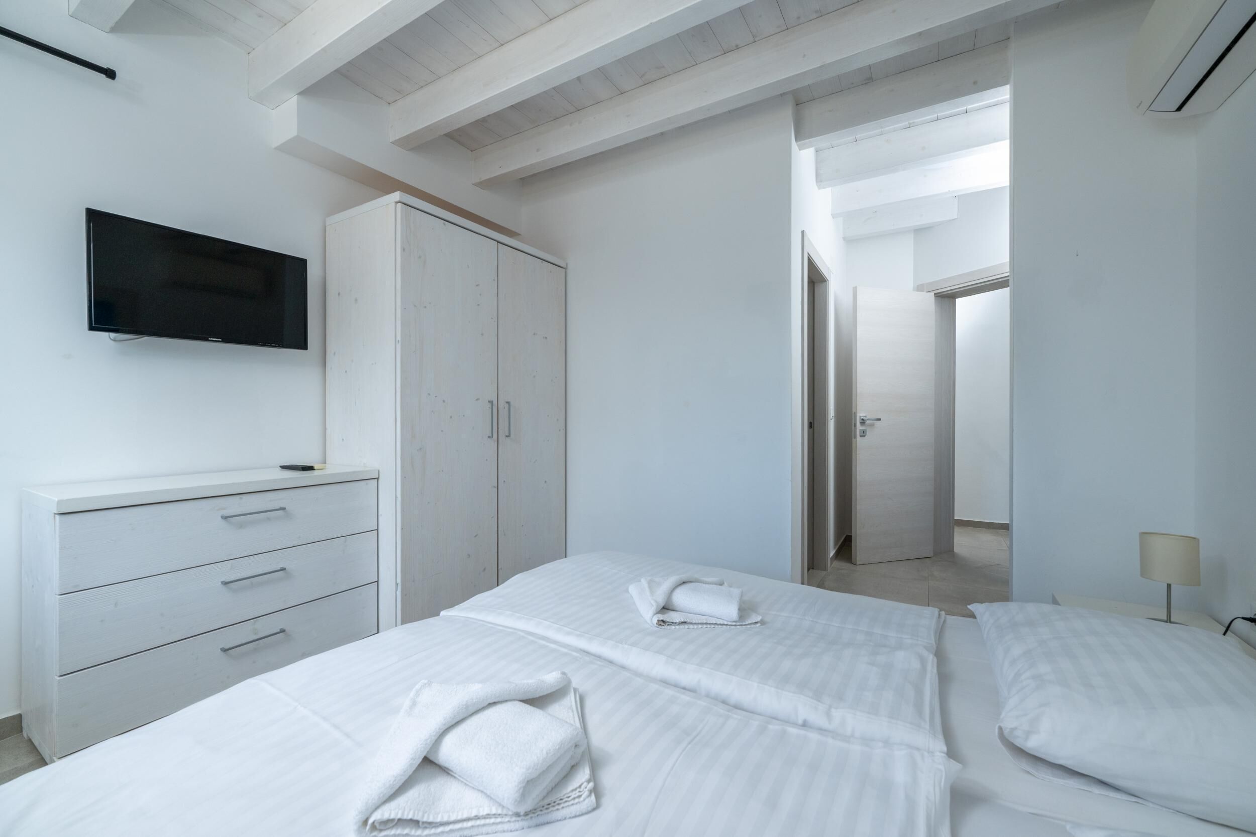 Habitació d'hotel moderna amb un llit gran, un armari, una televisió i un bany visible a través d'una porta oberta.