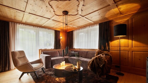 A cozy living room with a wooden ceiling, a leather armchair, a sofa, a coffee table with candles, and a floor lamp. - Residenz am Lech - Wohnung 1 (Steeg, Lechtal)