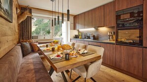 A modern kitchen with wooden cabinets, a dining area with a wooden table and chairs, and a large window offering a view of the outdoors. - Residenz am Lech - Wohnung 1 (Steeg, Lechtal)