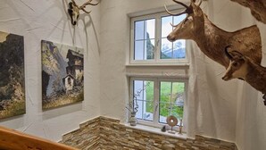 A room with a stone wall, a window with a view of greenery, and two mounted deer heads. - Residenz am Lech - Wohnung 3 (Steeg, Lechtal)