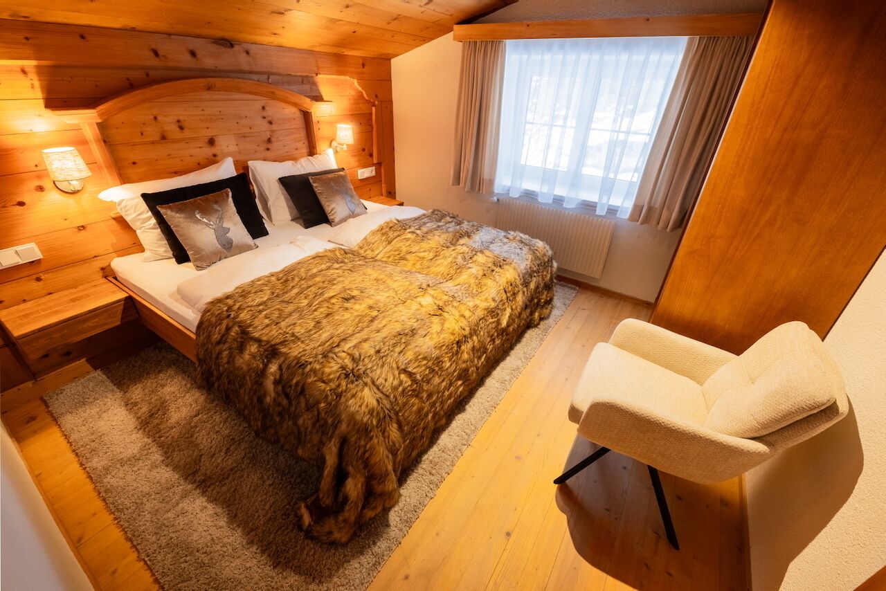 Una habitación acogedora de madera con una cama, una silla y un ventanal con cortinas.