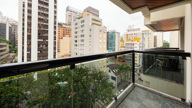Un balcón con vista a edificios de la ciudad, barandilla de vidrio y techo de madera.