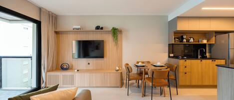 A modern living space with a sofa, dining area, kitchen, and a TV mounted on the wall.