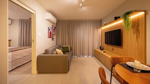 Una sala moderna con un sofá, una mesa de comedor con sillas, un televisor montado en la pared y una lámpara en el techo.