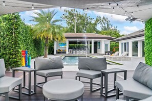 Relax in style with a pool area, lounge chairs, and a large screen for entertainment, surrounded by lush greenery.