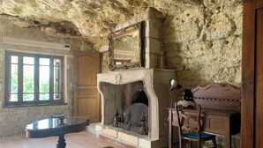 A rustic room with a stone wall, a fireplace, a wooden desk, and a chair.