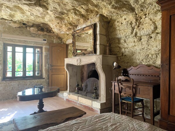 A rustic room with a stone wall, a fireplace, a wooden desk, and a chair.