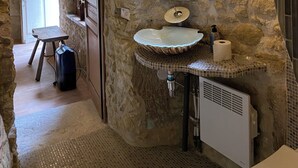 A rustic bathroom with a stone wall, a wooden door, a mirror, a sink, and a window.