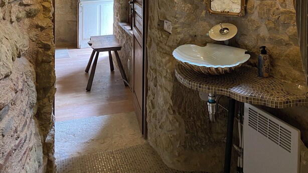 A rustic bathroom with a stone wall, a wooden door, a white sink, and a mirror.