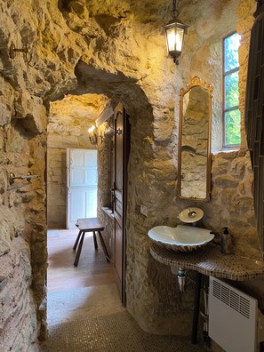 Ein rustikales Badezimmer mit einer Steinwand, einer Holztür, einem weißen Waschbecken und einem Spiegel.