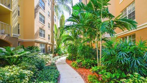 A pathway flanked by lush greenery and a building with multiple windows and balconies.